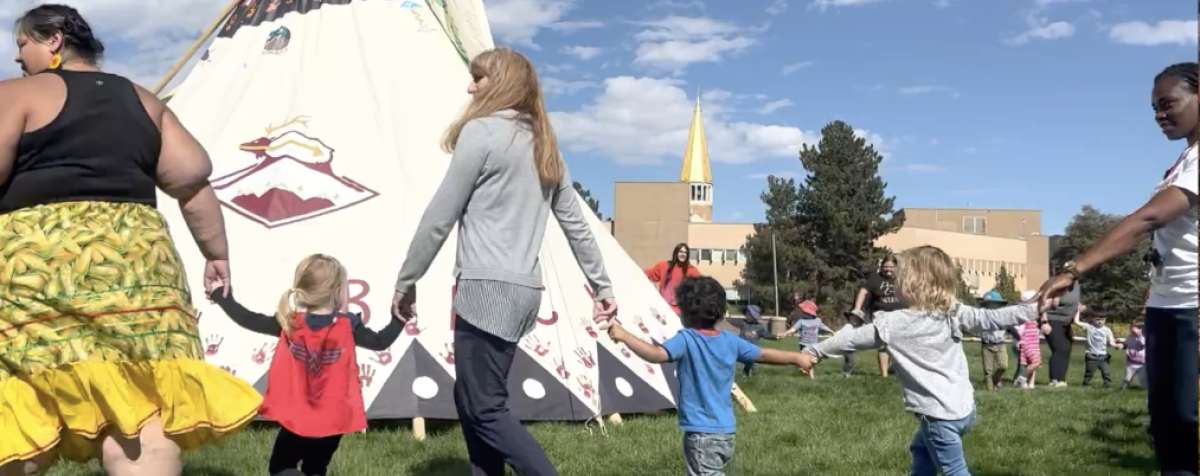 Campus Indigenous day, children and staff holding hands in a circle around Tipi 