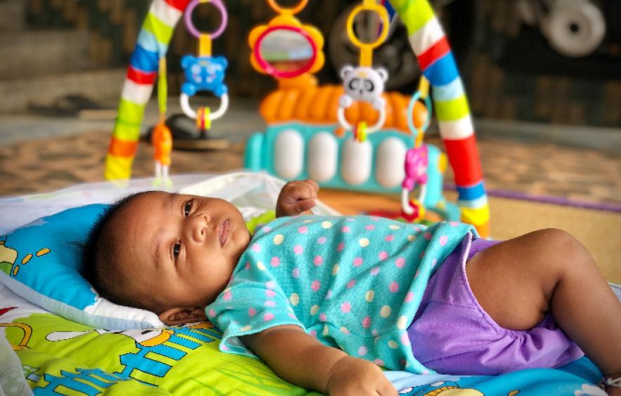 Baby laying on mat under toys