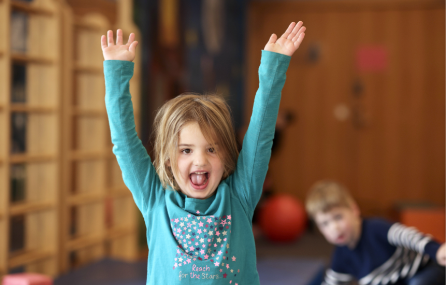 Child smiling with arms raised above her head