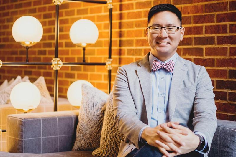 Sam Kim wearing blazer sitting with hands clasped
