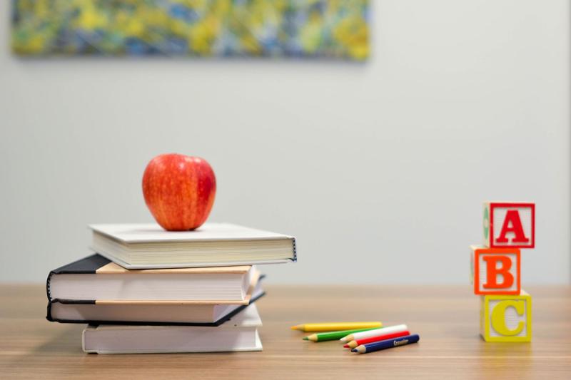 apple on stack of books next to colored pencils and a b c blocks on desk